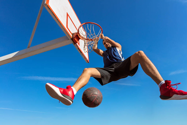 Slam Dunk. Side view of young basketball player making slam dunk - Foto, afbeelding