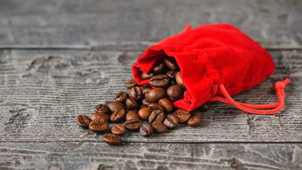 Ziarna kawy ciemno palona Kawa wylewa z czerwony worek na drewnianym stole. - Zdjęcie, obraz