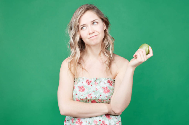 Zdrowe jedzenie i styl życia koncepcja. Ładna kobieta zjada apple, szuka nowej diety, jest zadowolony, aby stracić na wadze. Kobieta blonde pozowanie na nowym blogu wideo do sieci społecznościowych w tle zielony ściana . - Zdjęcie, obraz