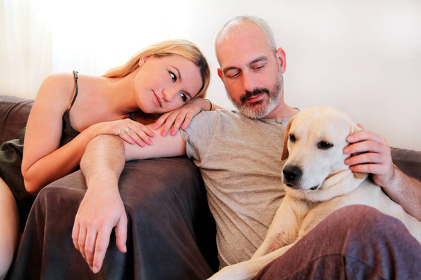 自宅で犬と人のカップル。恋人幸せとかわいいハンサムなカップルは家の居間で、黄色いラブラドル ・ レトリーバー犬の犬とお楽しみください。素敵な犬、かわいい犬は、かなり、ペット、家畜. - 写真・画像