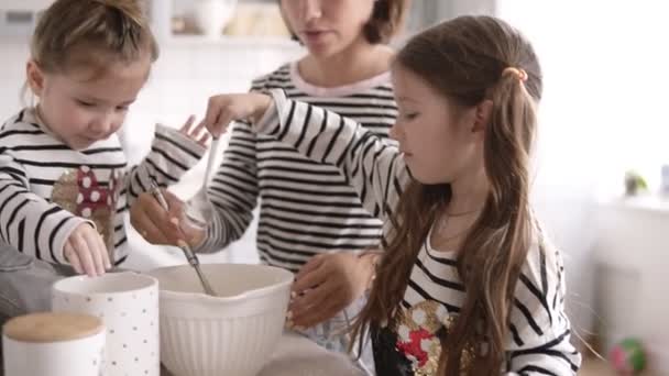 Girl with long brunette hair and her sister are helping their mother on the kitchen - Felvétel, videó