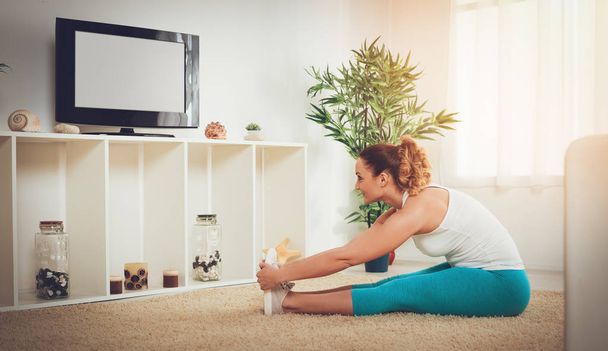 muscular smiling woman doing stretching exercise with online personal trainer on tv - Valokuva, kuva