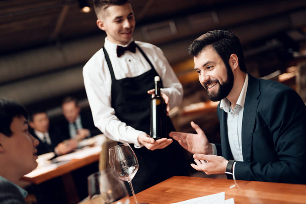 Waiter bringing wine to table on meeting with Chinese businessmen in restaurant - Фото, изображение