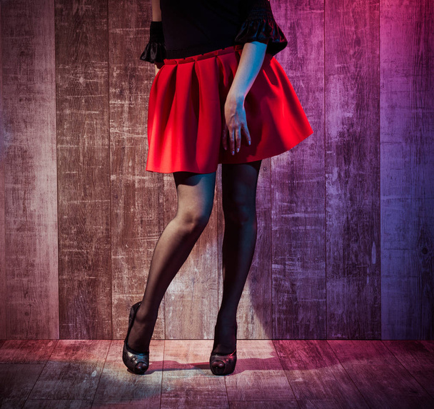 mladá žena nohy v černých punčochách a červenou sukni na dřevěné pozadí - Fotografie, Obrázek