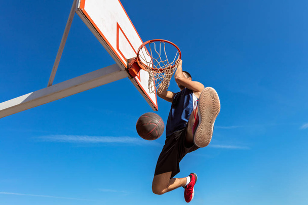 Slam Dunk. Side view of young basketball player making slam dunk - Fotografie, Obrázek