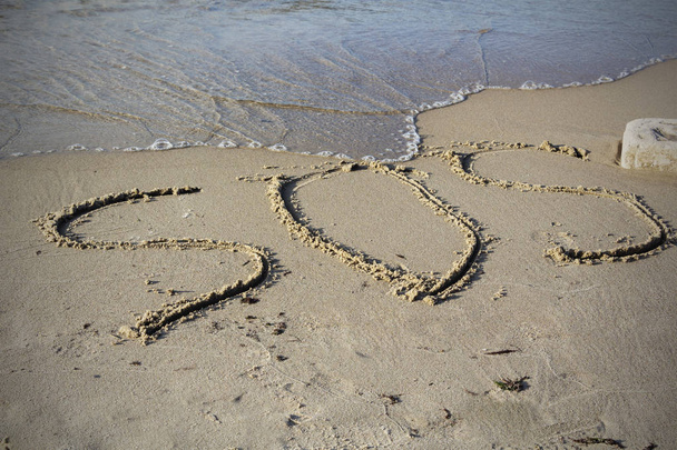 SOS - word drawn on the sand beach with the soft wave - Photo, Image