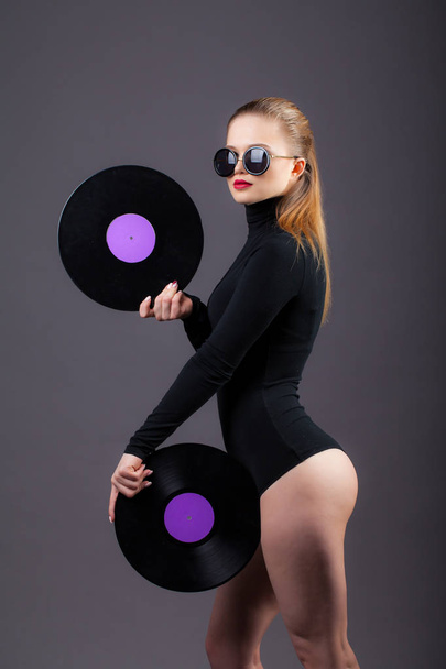A beautiful girl holds vinyl records in her sunglasses.  - Foto, Bild