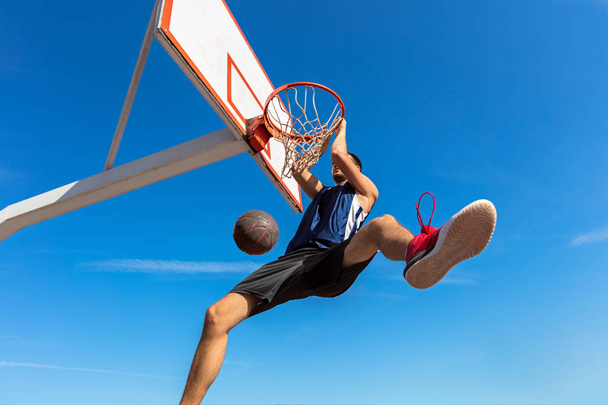 Slam Dunk. Side view of young basketball player making slam dunk - Φωτογραφία, εικόνα