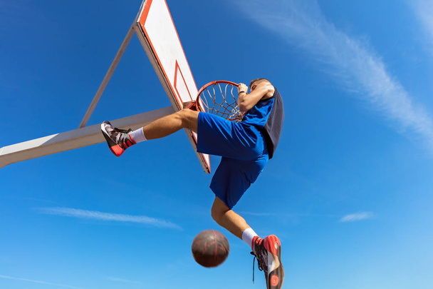 Slam Dunk. Side view of young basketball player making slam dunk - Photo, Image