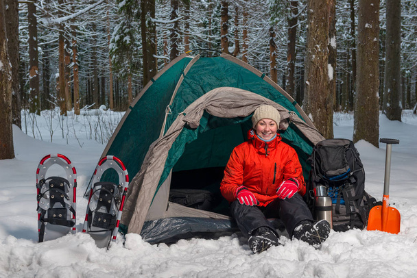 Gelukkig actieve toeristische zit in winter bos in de tent - Foto, afbeelding