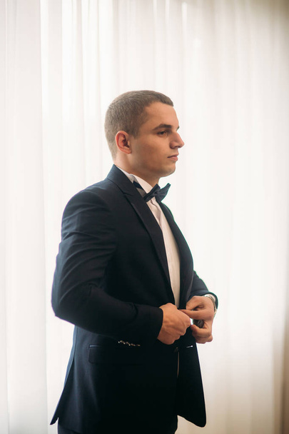 The groom is dressed at home in a suit. Cute groom posing for a photographer - Фото, зображення