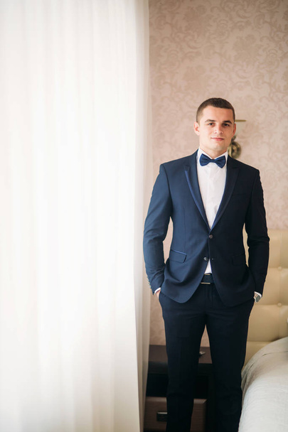 Handsome groom on a wedding day stand near the window - Foto, imagen
