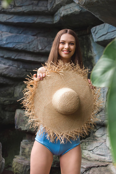 piękna kobieta uśmiechający się w słomkowym kapeluszu w tropikalnym ogrodzie - Zdjęcie, obraz