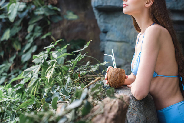 vista recortada de chica posando con coctel de coco en jardín tropical
 - Foto, imagen