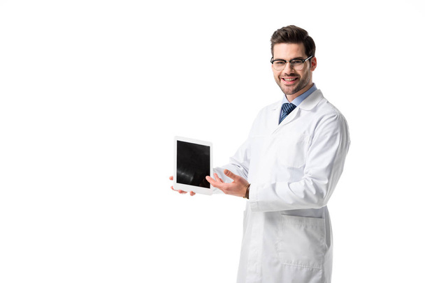 Smiling doctor wearing white coat presenting digital tablet isolated on white - Foto, afbeelding