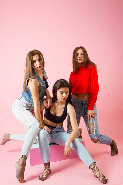 Three girls in jeans trousers on a bright background. Studio portrait - Foto, imagen