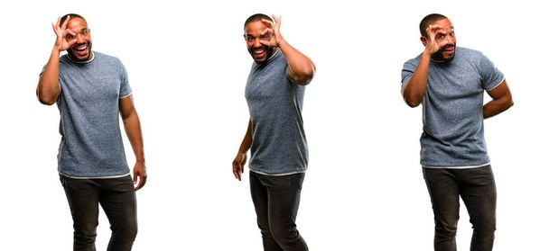 Африканский американец с бородой смотрит в камеру через пальцы в порядке жеста. Имитация бинокля, красивые глаза и улыбка
 - Фото, изображение
