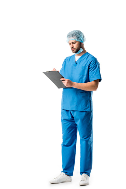 Travailleur médical réfléchi portant un uniforme bleu et écrivant dans un presse-papiers isolé sur du blanc
 - Photo, image