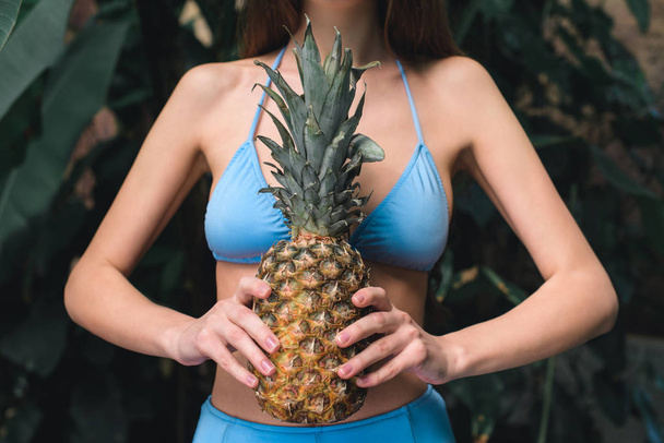 partial view of girl in blue bikini holding pineapple   - Фото, изображение