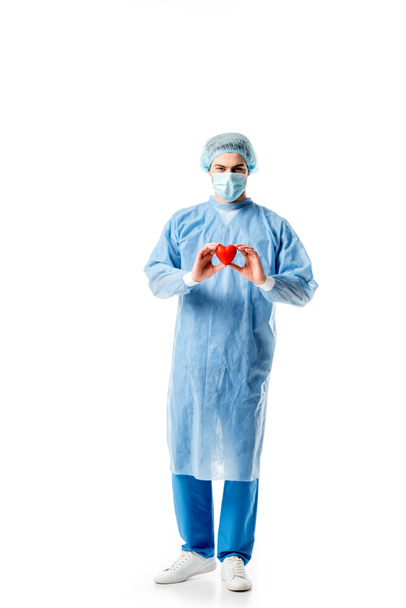 Cirujano vistiendo uniforme azul y sosteniendo corazón de juguete aislado en blanco
 - Foto, Imagen