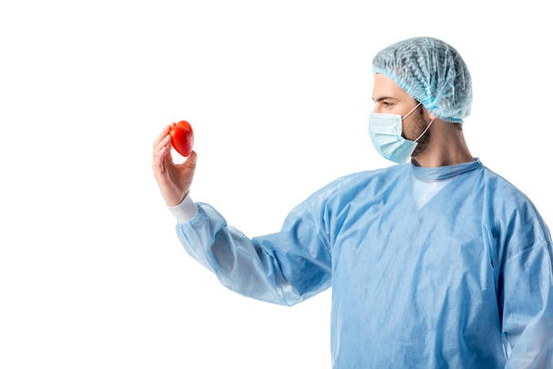 Cardiólogo concentrado con uniforme azul y corazón de juguete aislado en blanco
 - Foto, Imagen