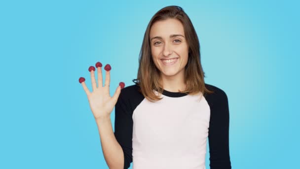 Pretty young woman eats raspberries from fingers - Video, Çekim