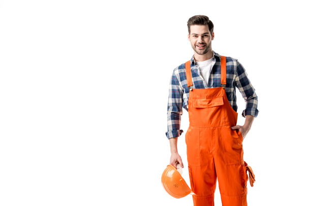 Smiling handyman in orange overall holding hard hat isolated on white - Photo, Image