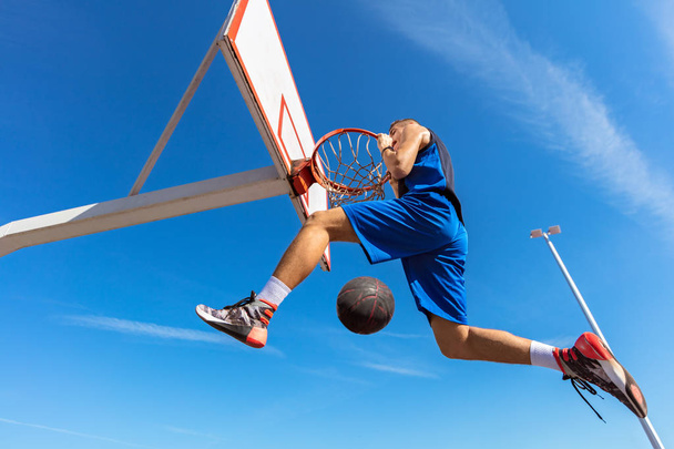 Slam Dunk. Side view of young basketball player making slam dunk - Foto, afbeelding