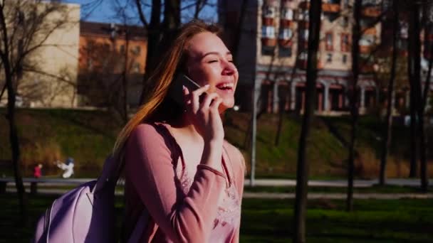 Vrolijke student in park lopend en pratend door smartphone in slow motion. - Video