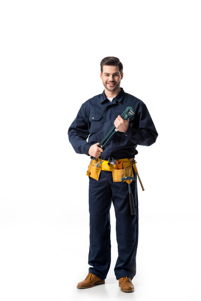 Confident handyman wearing uniform with tool belt and holding wrench isolated on white - Photo, Image