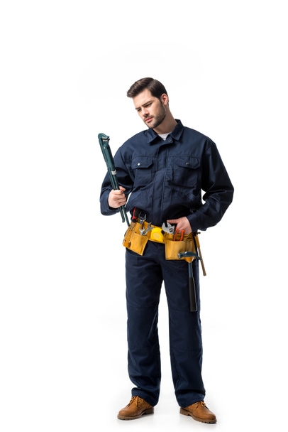 Young handyman wearing uniform with tool belt and looking at wrench isolated on white - Fotoğraf, Görsel