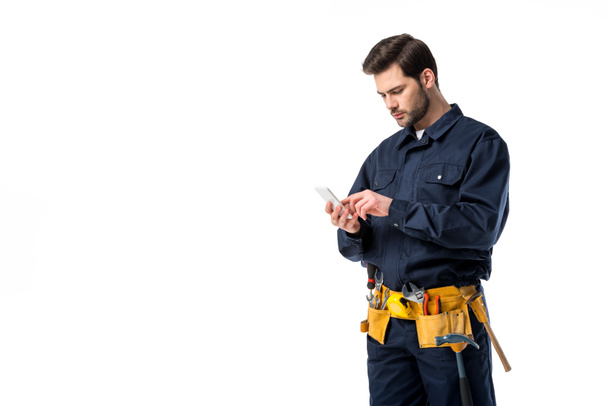 Fontanero profesional con cinturón de herramientas usando smartphone aislado en blanco
 - Foto, imagen