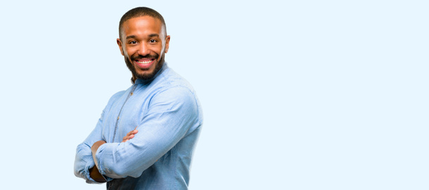 Hombre afroamericano con barba con brazos cruzados confiado y feliz con una gran sonrisa natural riendo aislado sobre fondo azul
 - Foto, Imagen