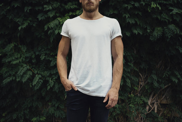 young man in white t-shirt against green plants background - 写真・画像