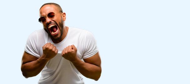Hombre afroamericano con barba feliz y emocionado celebrando la victoria expresando gran éxito, poder, energía y emociones positivas. Celebra nuevo trabajo alegre aislado sobre fondo azul
 - Foto, Imagen