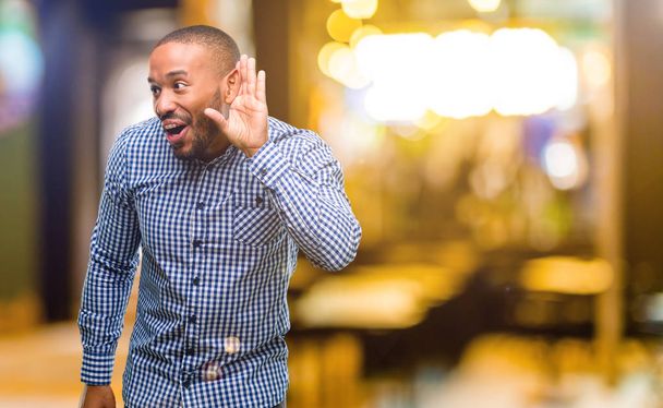Afrikanisch-amerikanischer Mann mit Bart, der die Hand am Ohr hält und versucht, interessante Nachrichten über Kommunikationskonzept und Klatsch in der Nacht zu hören - Foto, Bild