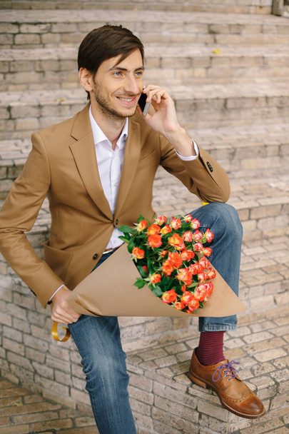 Красивий чоловік тримає букет з троянд, що розмовляють щасливо по телефону
 - Фото, зображення