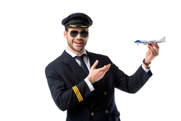 retrato de piloto barbudo sonriente en uniforme apuntando al avión de juguete en mano aislado en blanco
 - Foto, Imagen