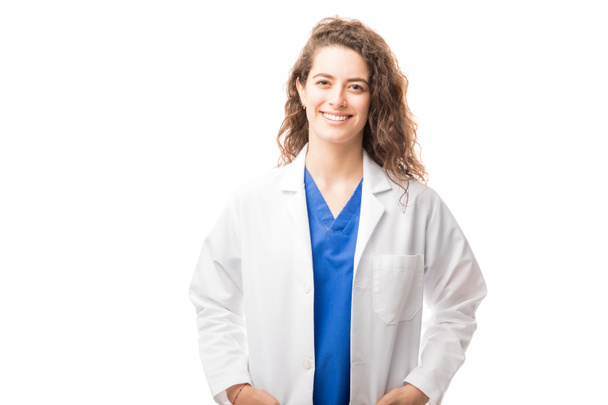 Portrait of a good looking female doctor wearing a lab coat and smiling isolated on white background - 写真・画像