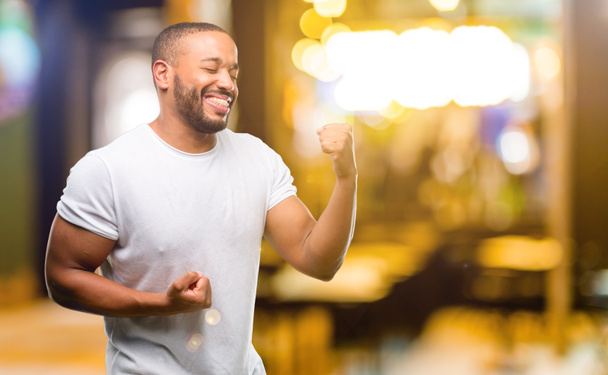 African american man with beard happy and excited celebrating victory expressing big success, power, energy and positive emotions. Celebrates new job joyful at night - Photo, Image