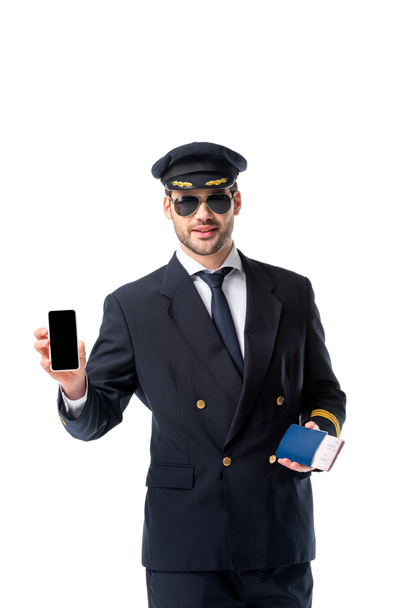 πορτρέτο του πιλότου σε ομοιόμορφο με διαβατήριο και εισιτήριο στο χέρι δείχνοντας smartphone με κενή οθόνη που απομονώνονται σε λευκό - Φωτογραφία, εικόνα