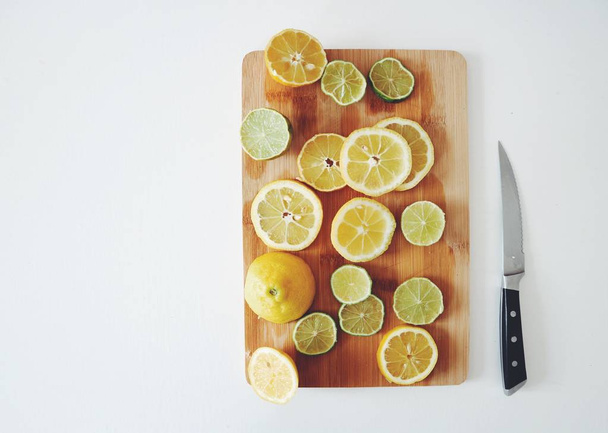 close-up photo of sliced lemons on wooden board with knife on white table background - Photo, Image