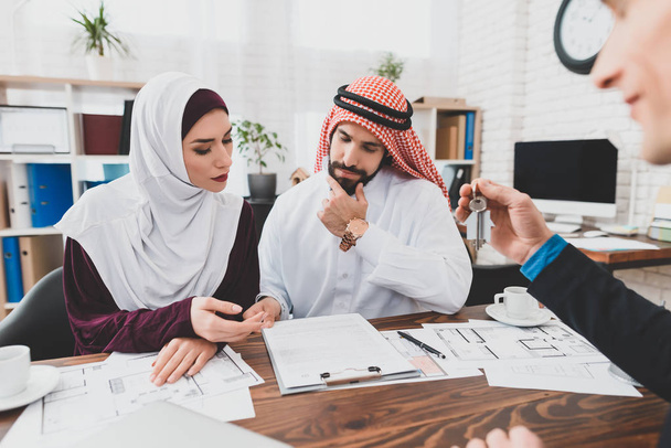 Arab couple in national clothes reading contract of sale thoughtfully at real estate agency - 写真・画像