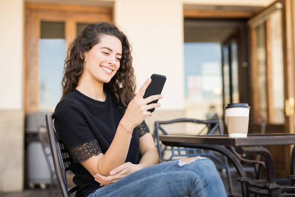 young caucasian girl sitting at cafe and using her smart phone - Foto, afbeelding