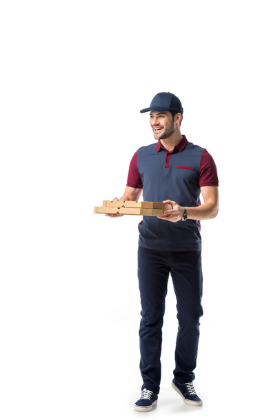 smiling delivery man with cardboard pizza boxes looking away isolated on white - Fotó, kép