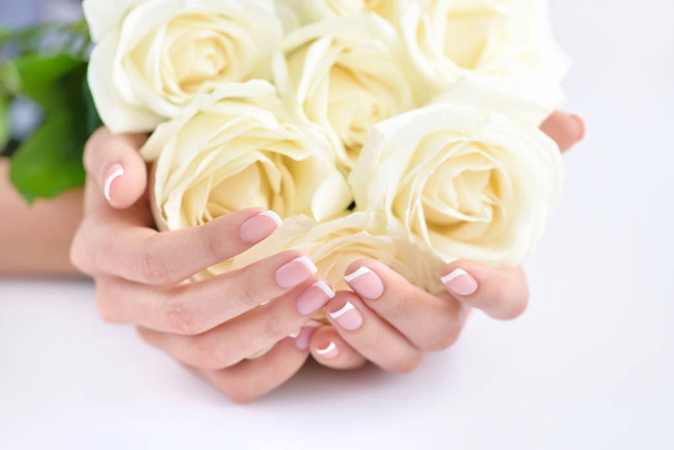 Hände einer Frau mit schöner französischer Maniküre und weißen Rosen - Foto, Bild