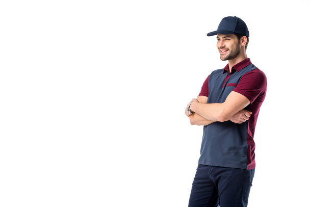 side view of smiling delivery man in cap with arms crossed isolated on white - Foto, afbeelding