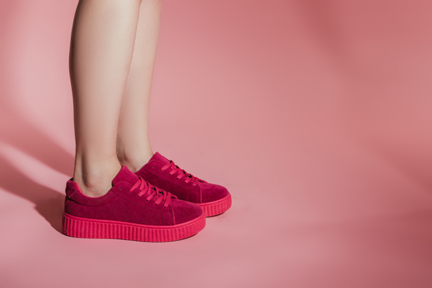 cropped image of woman legs in stylish sneakers on pink background - Fotó, kép