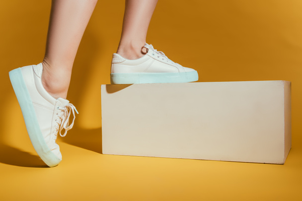 cropped image of woman feet in stylish sneakers on yellow background - Photo, Image