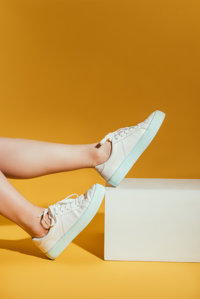 cropped image of woman feet in stylish sneakers on yellow background - Photo, Image